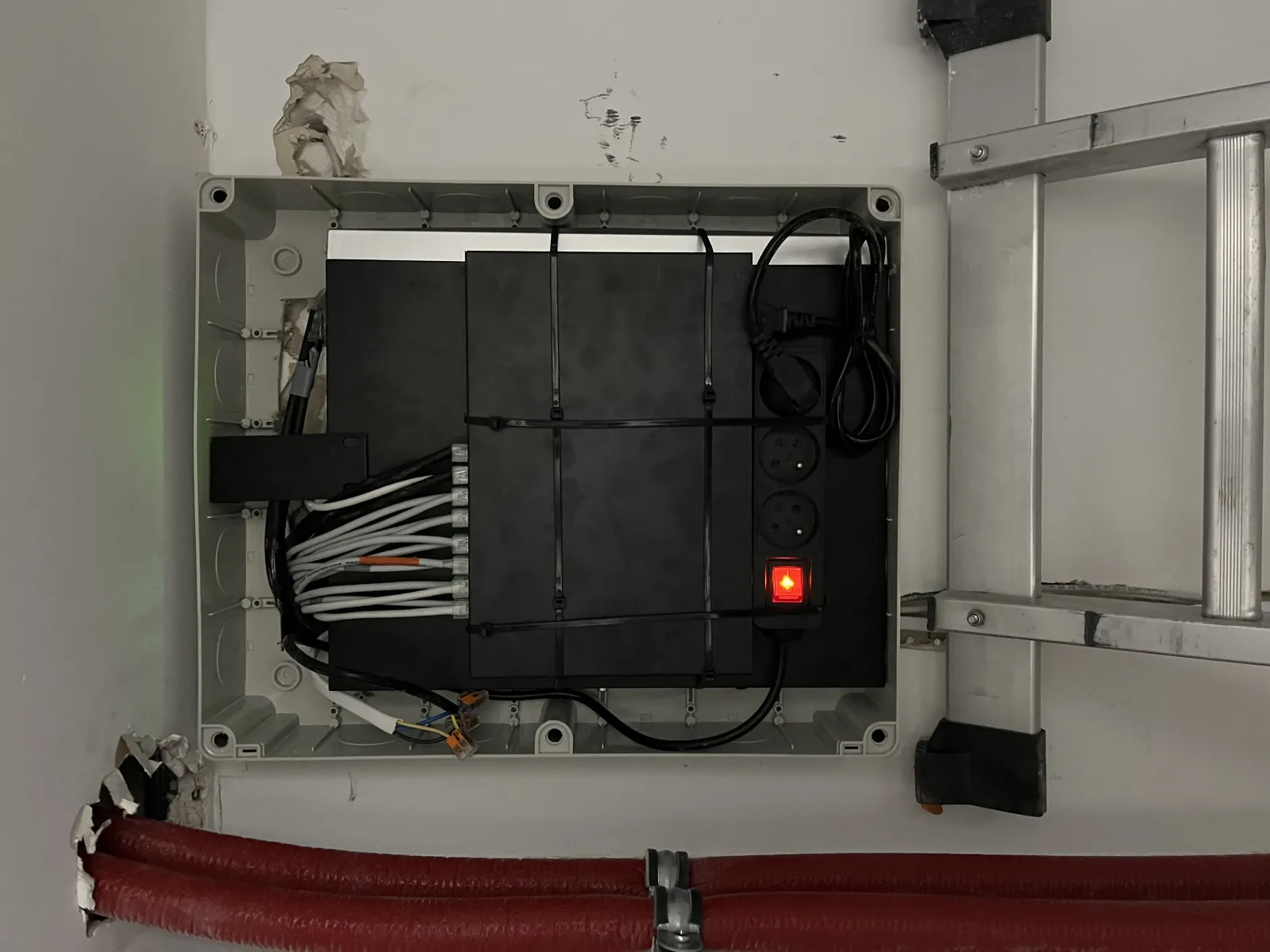 Perfekcyjnie uporządkowane wnętrze szafki instalacyjnej z rejestratorem i listwą zasilającą.